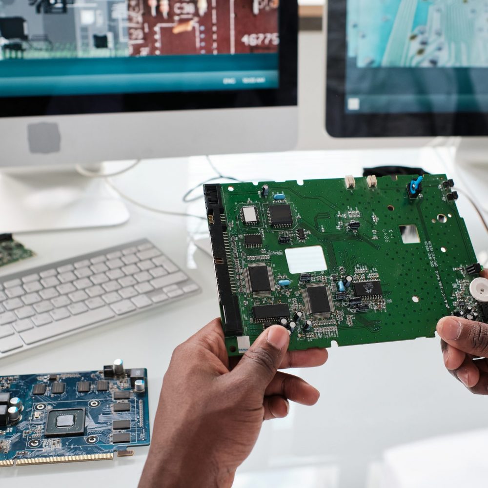 Hands of young African scientist holding part of electronic device with microchips over workplace